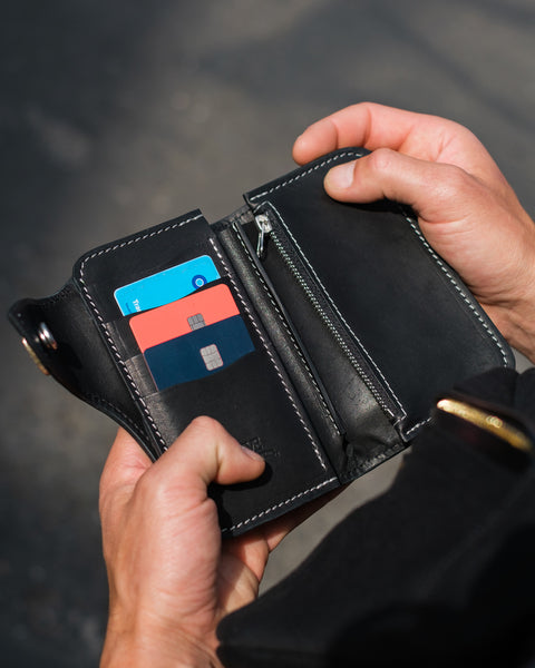 Black leather wallet with cards held open by a hand against a blurred background