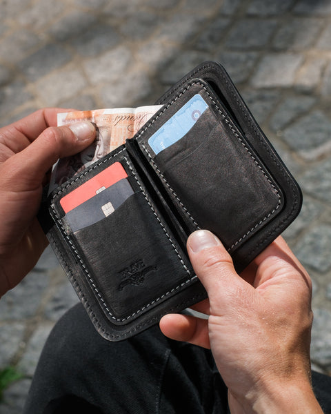 Person holding a black leather wallet with cards and money against a stone pavement background