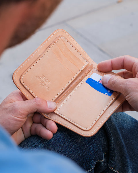 Person holding a Obbi Good Label Natural leather wallet with a card inside, sitting on a wooden surface.