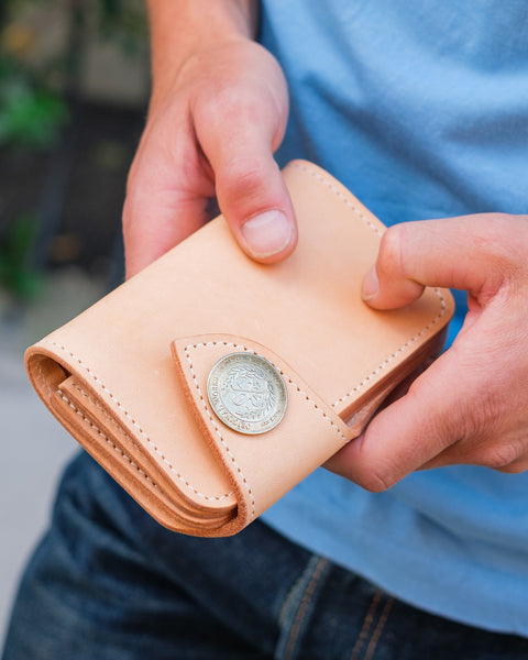 Person holding a beige leather wallet with a coin on a blurred background