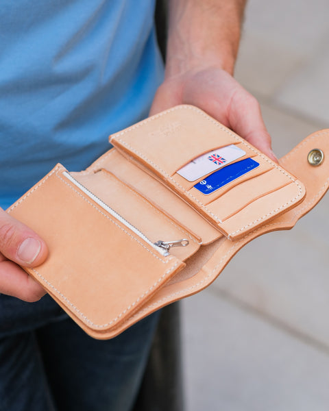 Person holding a beige leather wallet with a card inside, blurred background