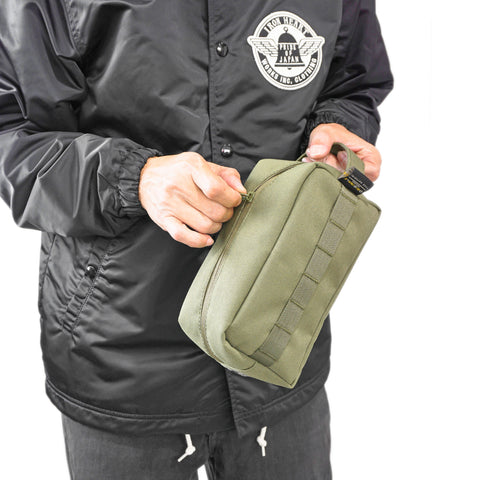 Model carrying ORIGO Utility Dopp Kit in olive abrasion-resistant technical canvas with zippered compartment, grab handle by Obbi Good Label in Rugged Gentlemen Shoppe Singapore