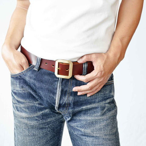 Model wearing OGL Single-Prong Garrison Leather Belt Hand-Dyed Brown with solid brass buckle, Unique Patina with faded raw denim jeans